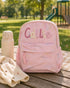 Personalized pink quilted kids backpack with custom name embroidery on an outdoor picnic table