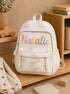 Personalized white quilted kids backpack with colorful custom name embroidery in a warm nursery setting