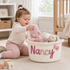 Cute baby playing next to a soft MamaRaya personalized cotton rope gift basket filled with newborn essentials.